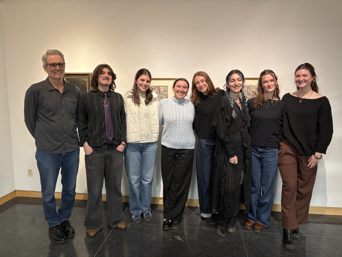 A professor stands alongside a group of students in an art gallery.