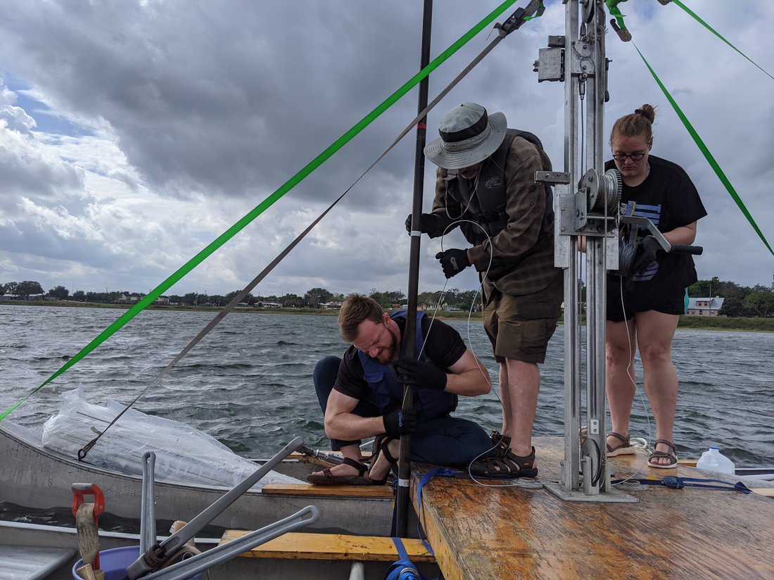 Three people on a lake capturing sediment cores.