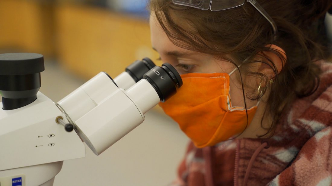 women wearing Covid mask looking through microscope