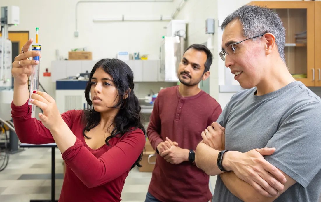 Three people in a lab with one holding a syringe.