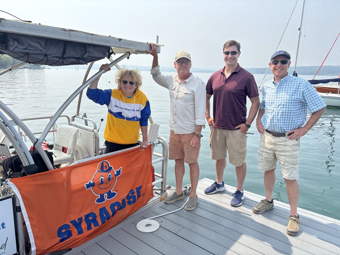 Group of people standing on a dock with a boat and lake in the background.