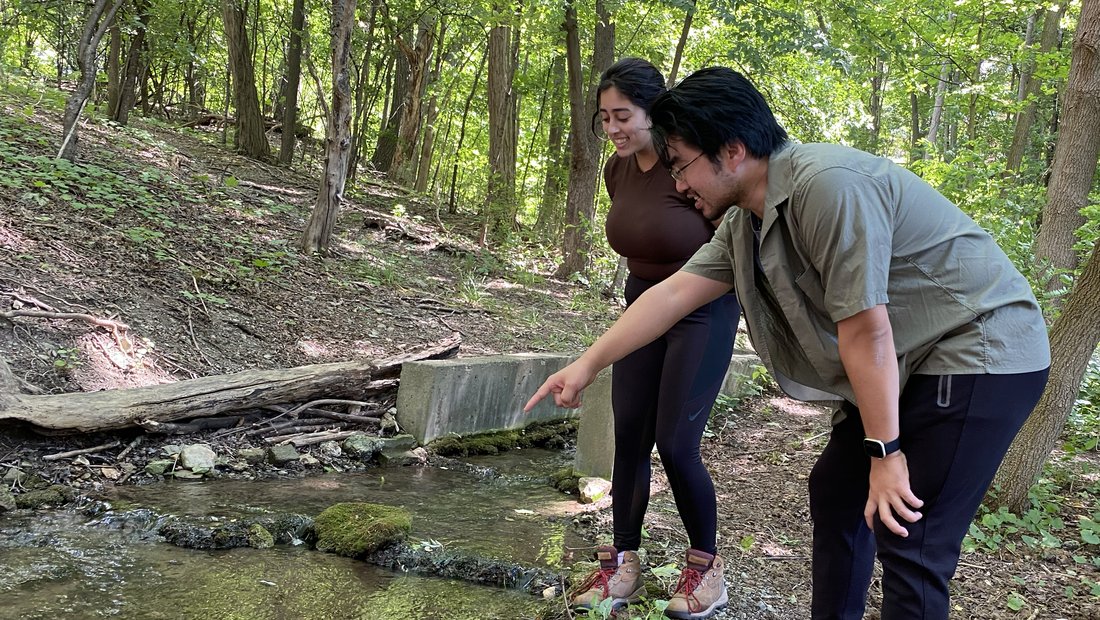 Two people standing beside a creek.