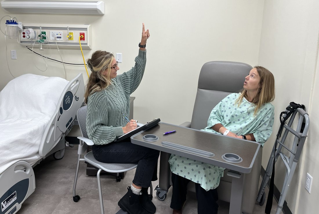 One person holding up a finger and another person looking up while seated in a simulated medical lab.