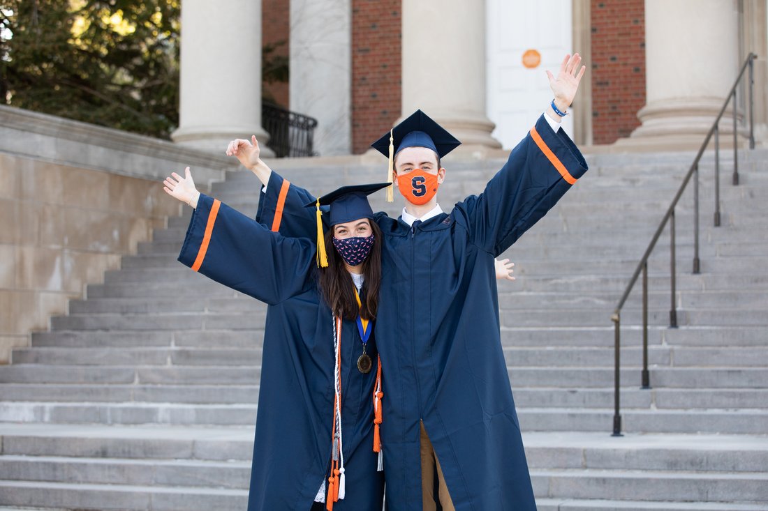 Two people in caps and gowns with masks.