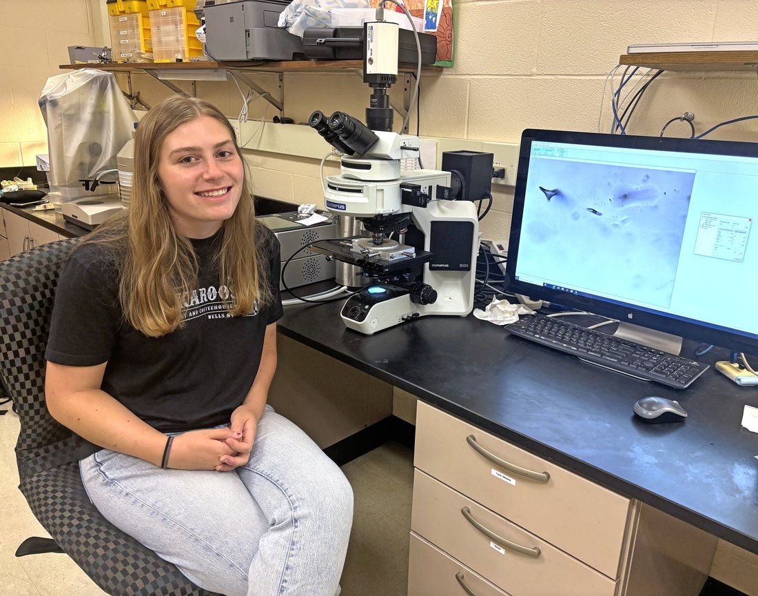 Perosn posing for a photo with a microscope and a computer screen.