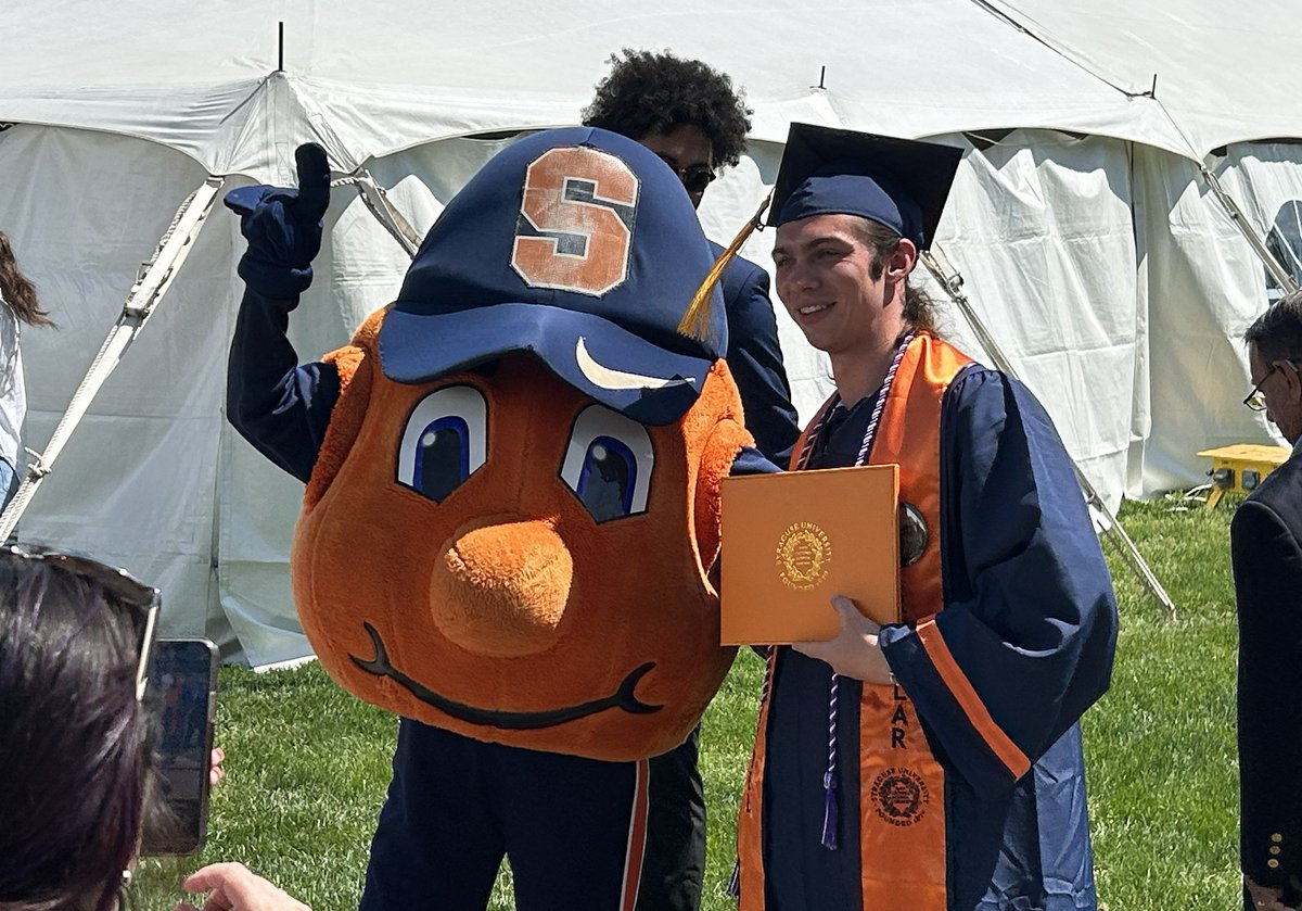 Graduate taking a photo with Otto the Orange outside durning 2023 Commencement.