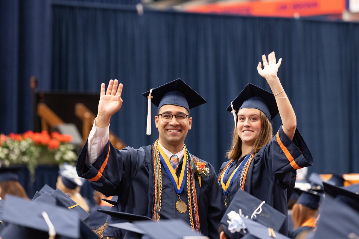 Two graduating students waving and smiling in their cap and gowns.