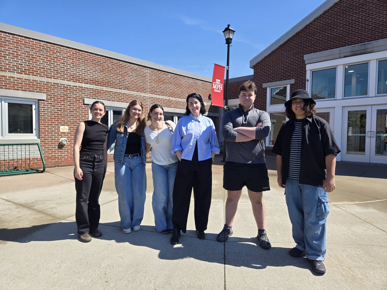 Teacher and students standing outside a school.