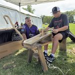 Two people working together to carve a lacross stick.