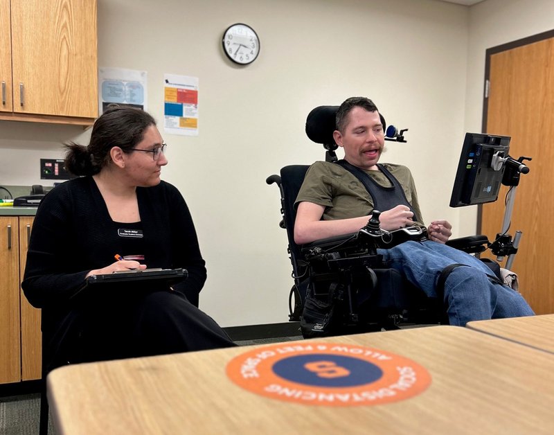 Person sitting with a notepad next to a person in a wheelchair.