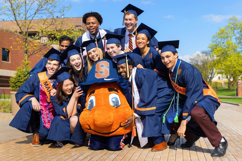 a group of undergraduate students in caps and gowns with otto the orange