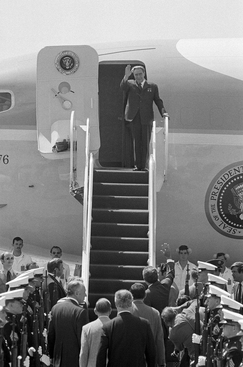 Person walking off a plane waving to a crowd.
