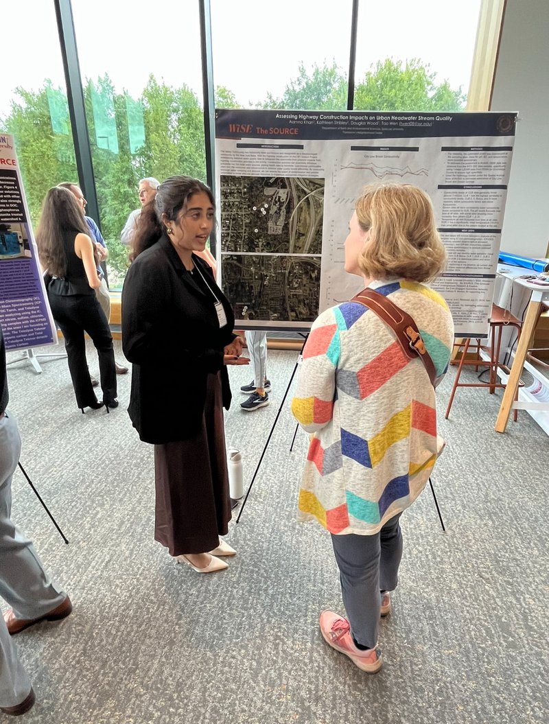 Two people talking in front of a poster.