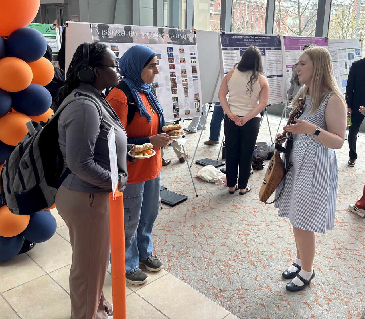 Three people standing and talking with one holding a stringed instrument.