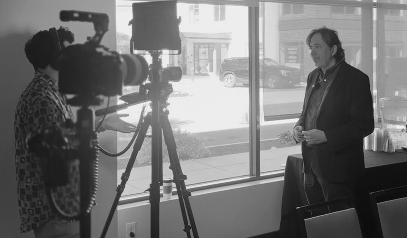 Person being interviewed with camera equipment in the foreground.