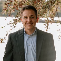 Brett Jakubiak in a gray suit and blue shirt. With fall leaves in the background.