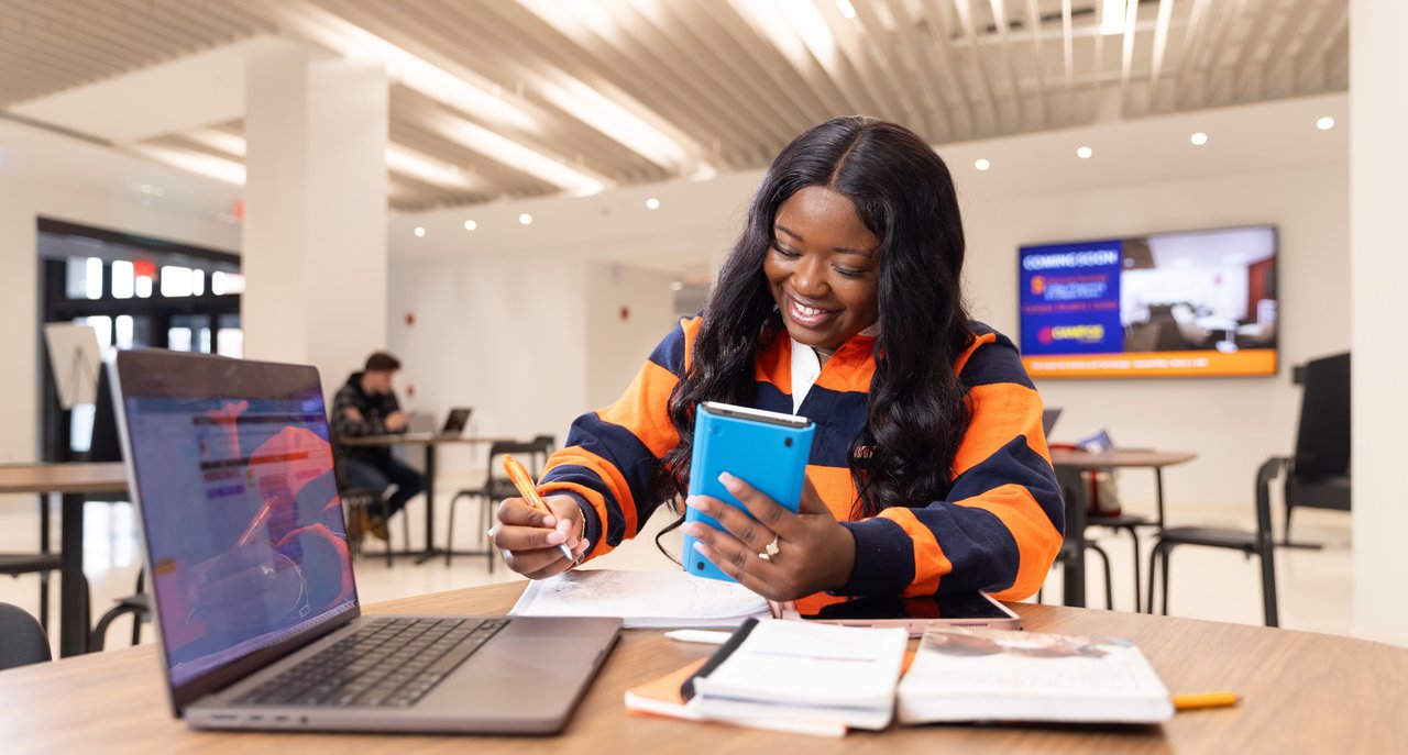 Person holding a cell phone with a computer in the foreground.