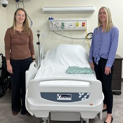 Two people standing beside a hospital bed.