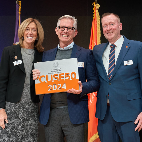 Three people standing together with one person holding an award.