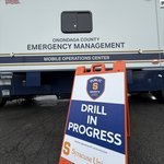 A sign reads "Drill In Progress" in front of an Emergency Management van