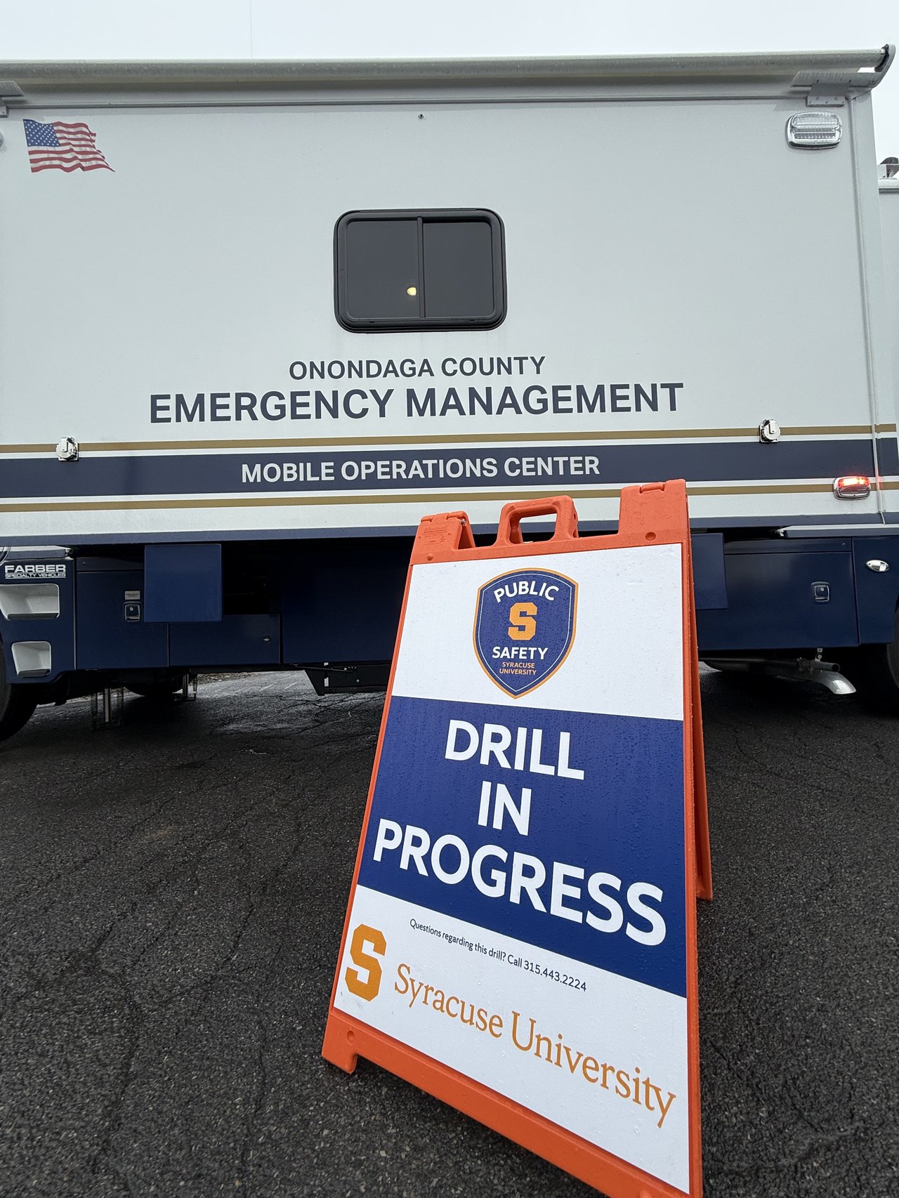 A sign reads "Drill In Progress" in front of an Emergency Management van
