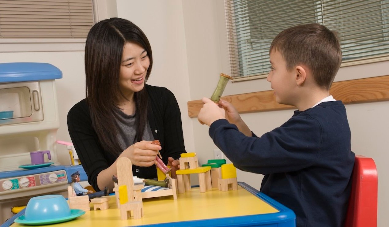 An adult playing with a child during therapy session.