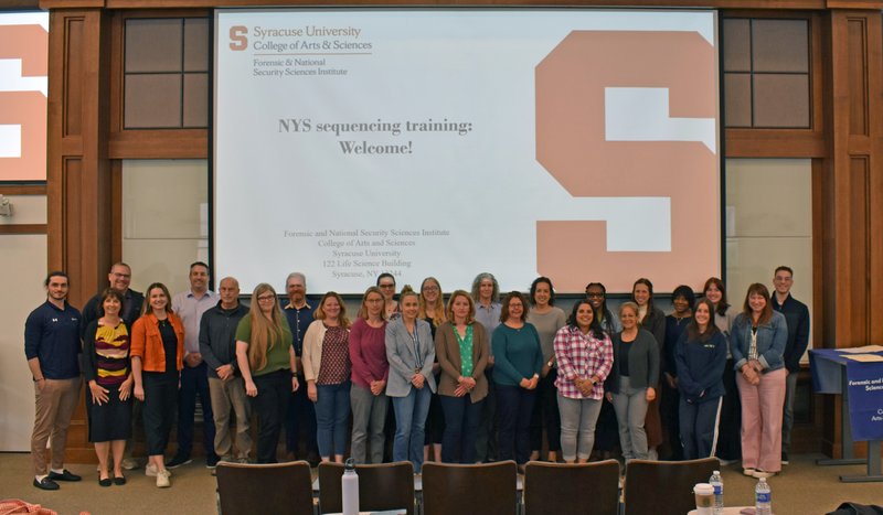 Group of people standing in front of a projection screen.