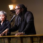 A man speaking at a podium with a woman looking on.