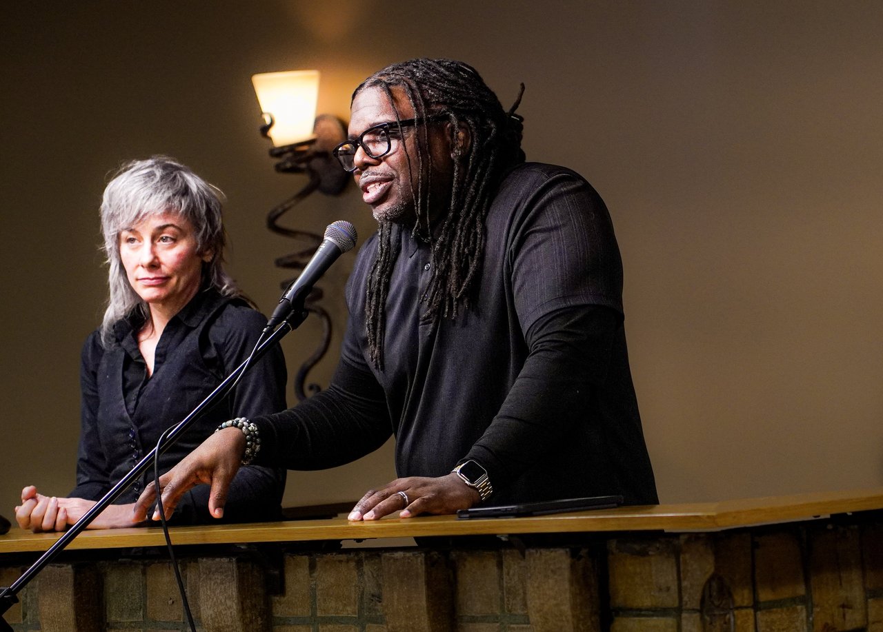 A man speaking at a podium with a woman looking on.