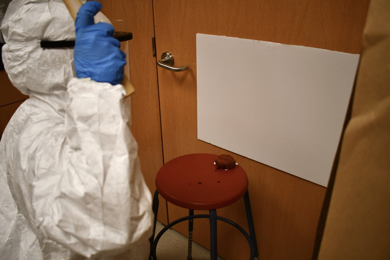 A person in a hazmat suit flinging red paint onto a poster board.