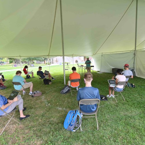 Denver teaching a class in a tent.