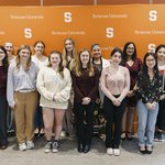 Group of people standing in front of a Syracuse University orange banner.