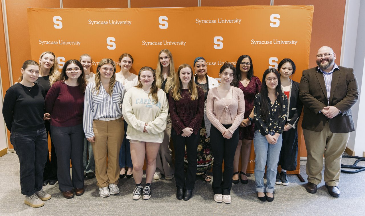Group of people standing in front of a Syracuse University orange banner.