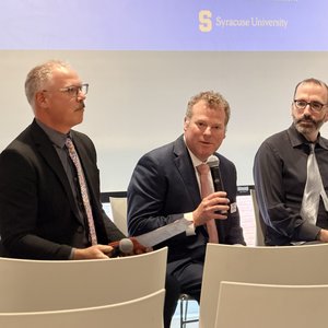 Three people sitting on a panel with one talking into a microphone.