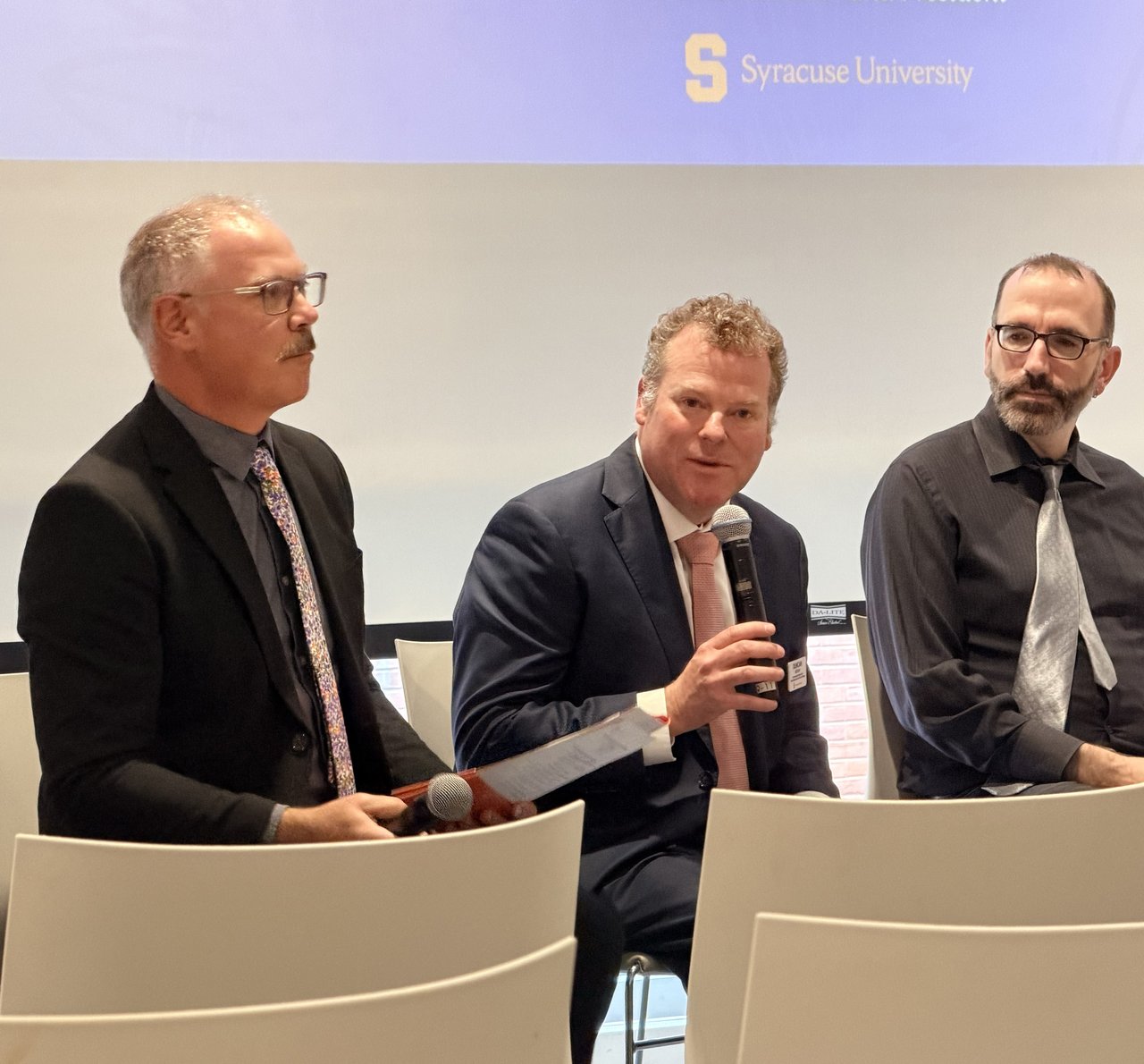 Three people sitting on a panel with one talking into a microphone.