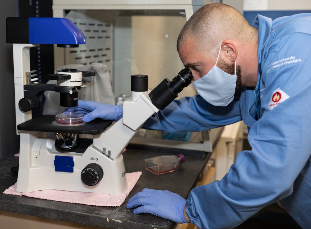 A research student looking at cells under a microscope in the lab.