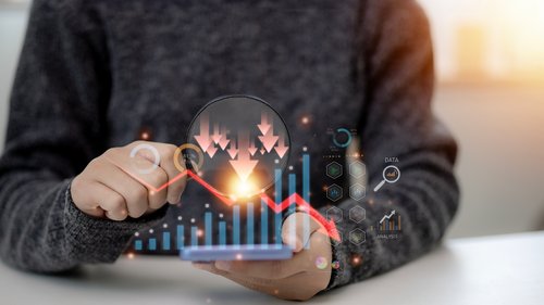 Person sitting at a desk holding a phone with superimposed graphics of economic downturn.