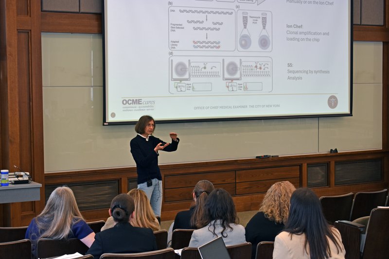 Person addressing a group in front of a projection screen.