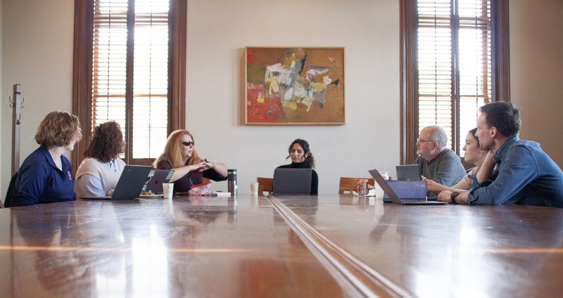 Seven faculty and staff members engage in dialogue while sitting around a table.