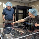 Person pointing at an optical table with two others looking on.