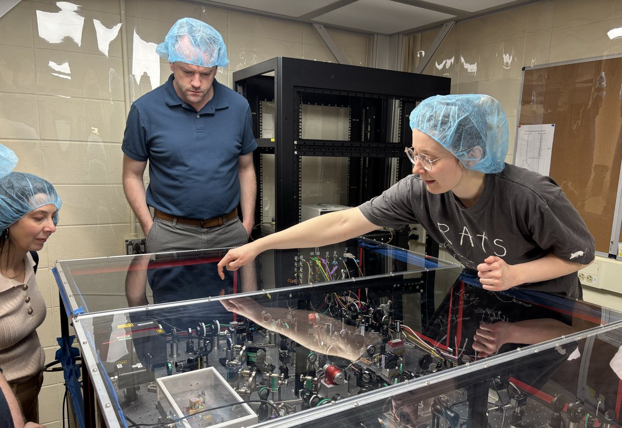 Person pointing at an optical table with two others looking on.