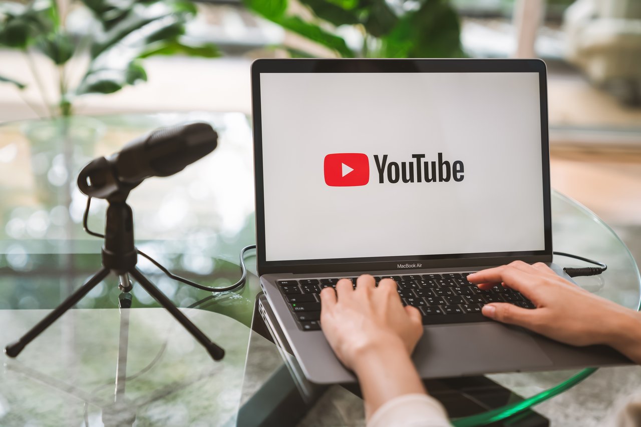 Hand using a laptop with screen displays the Youtube app icons on Apple Macbook Air.