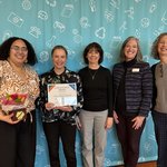 Five women standing in a row, with one holding an award.