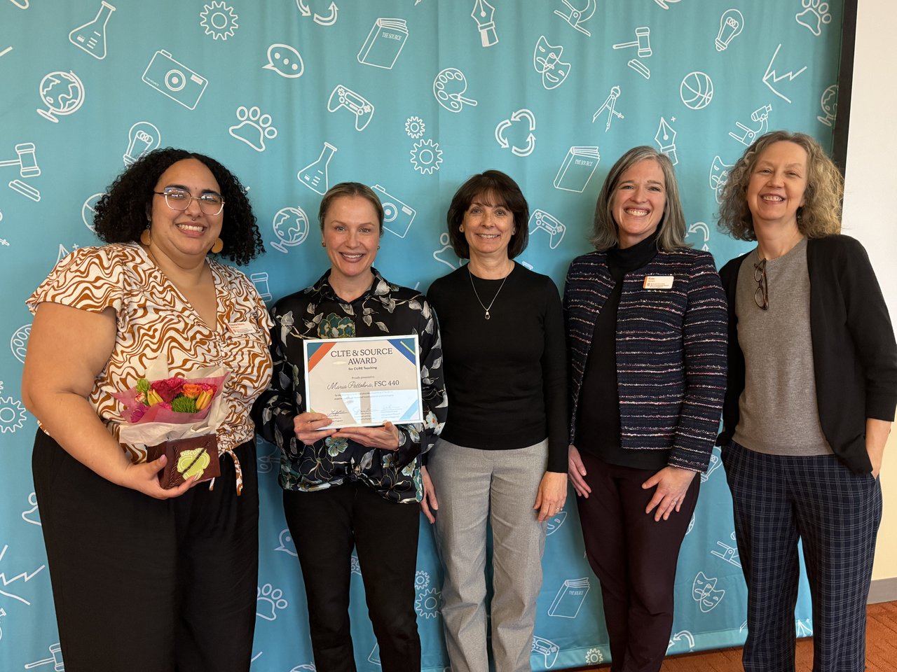 Five women standing in a row, with one holding an award.