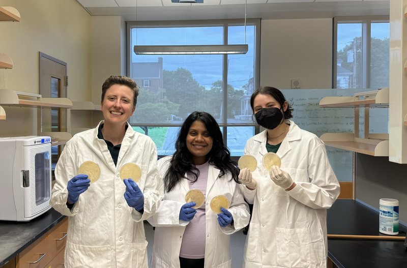 Three people in lab coats holding petri dishes.