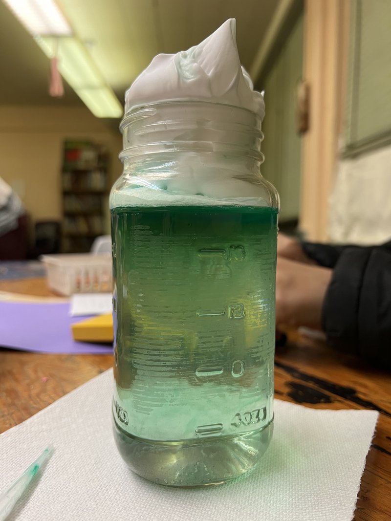 Jar with green water and shaving cream on top.
