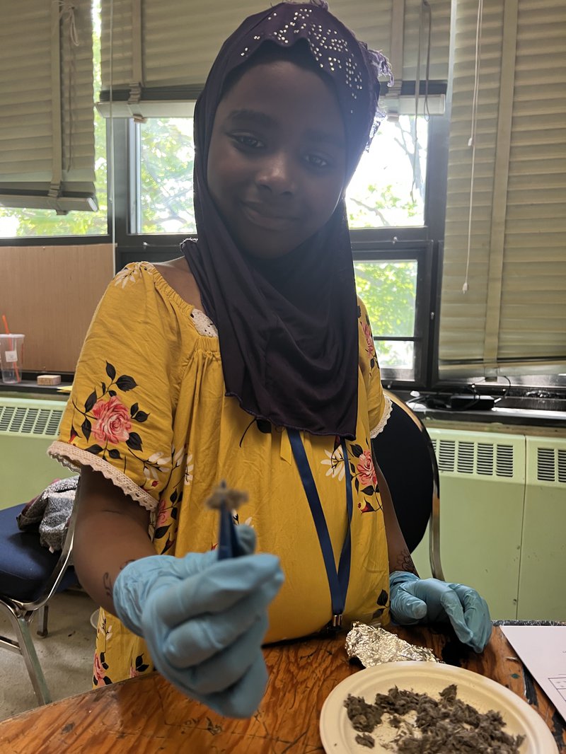 Girl showing a piece of owl pellet with tweezers and blue gloves.