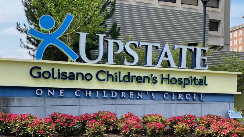 An exterior sign for Upstate Golisano Children's Hospital at One Children's Circle, surrounded by pink flowers in bloom.