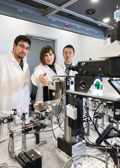 Three people in lab coats in a lab with lab equipment in the foreground