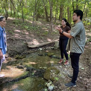 Three people talking beside a stream.